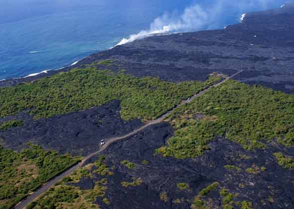 Overhead view from northeast  of west end of access road, showing lava flowing over last unpaved segment; third and fourth paved segments; and unpaved segment with pullout and parked car linking those two paved segments