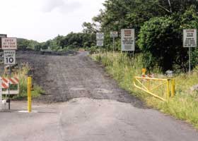 At end of pavement, open yellow gate at entrance to narrow gravel road, lined my multiple warning signs