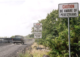 Set of three warning signs: in foreground, 'Caution | Be aware of | pedestrians'; in background, 'Caution | Hazardous and | closed area | ahead | Obey all signs' and 'No alcoholic | beverages | allowed'