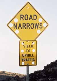 Warning signs: 'Road Narrows' and 'Yield to Uphill Traffic'; each sign with six holes