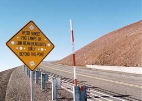 Warning sign with multiple holes: 'After Sunset | Fog Lamps Or Low Beam Headlights Only Beyond This Point'