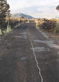 Road with patchy pavement, and irregular thin fog line down the middle