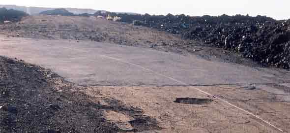 Potholed pavement transitions to smooth pavement turning to the left, unpaved road veering off straight ahead