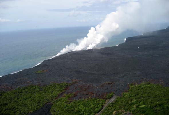 Overhead view from northeast  of new west end of access road, showing solidified lava covering part of last unpaved segment; steam plumes indicate where lava is flowing into the ocean